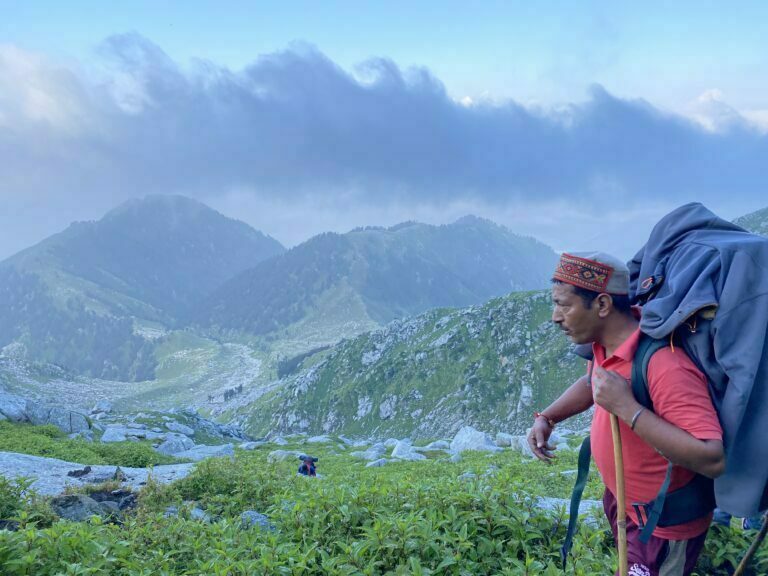 Local guide carrying supplies across an alpine meadow