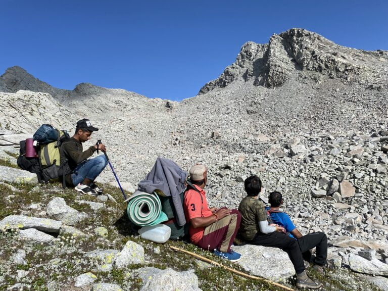 Trekkers resting on a rocky high-altitude Dhauladhar trail