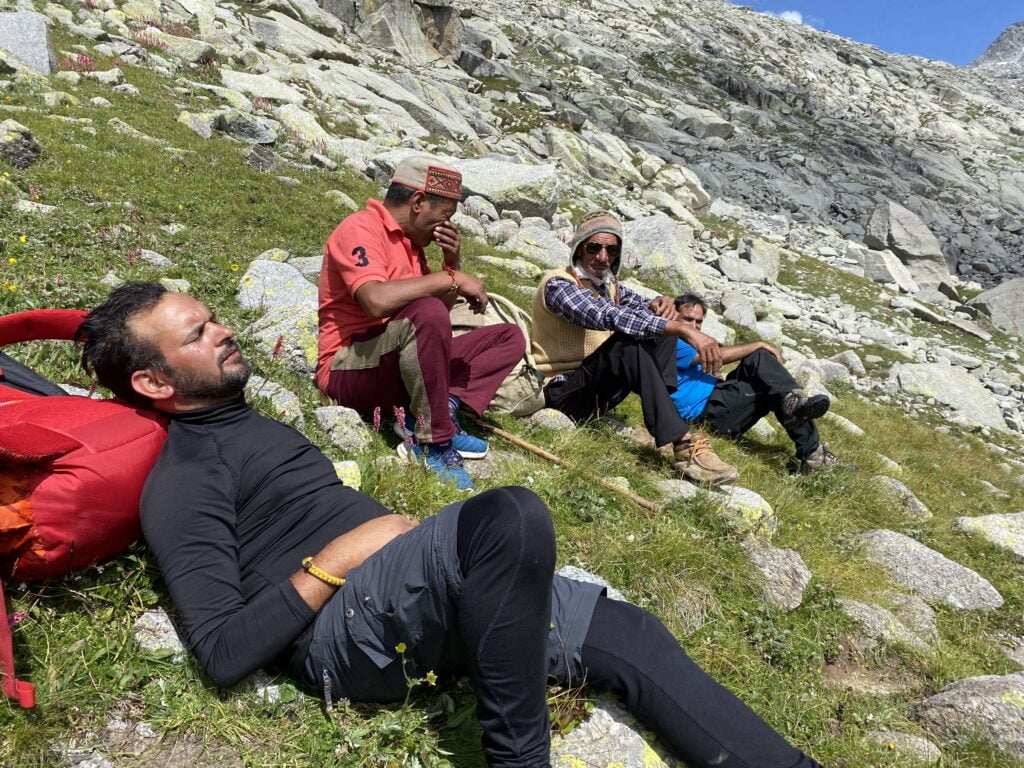 Group of trekkers resting on a rocky hillside during a Himalayan trek in the Dhauladhar mountains near Dharamshala