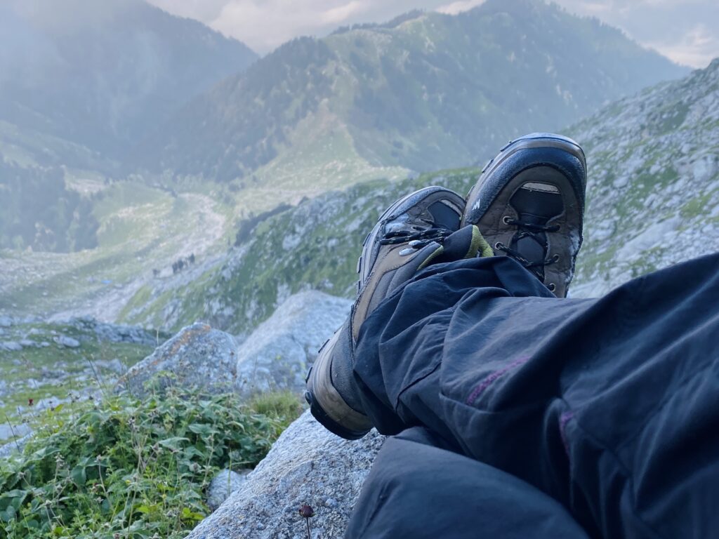 Trekker resting on a rock with hiking boots during the Seven Lakes Trek in the Dhauladhar range near Dharamshala