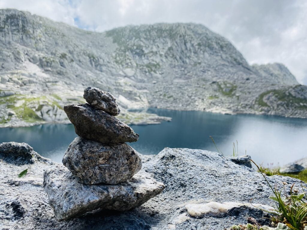 Stone cairn beside a high-altitude alpine lake on the Seven Lakes Trek in the Dhauladhar range near Dharamshala