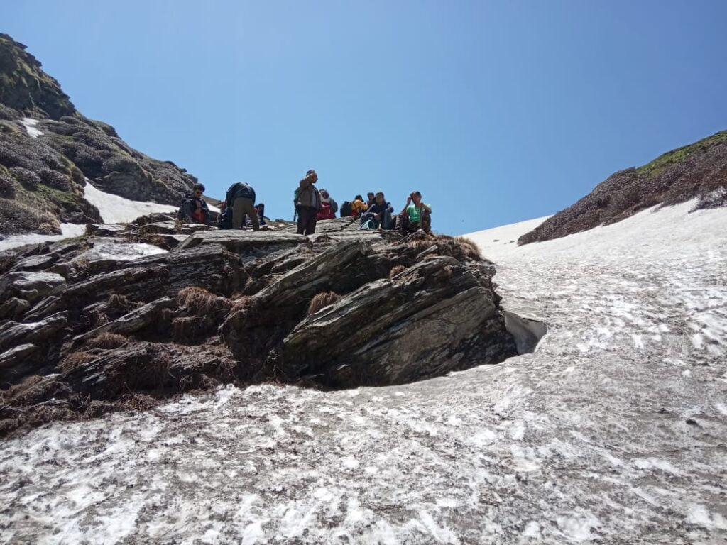 Trekkers resting on rocks beside snow on the Jalsu Pass route