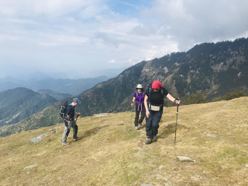 Trekkers walking on a grassy Himalayan ridge during a Dharamsala trek in Himachal Pradesh