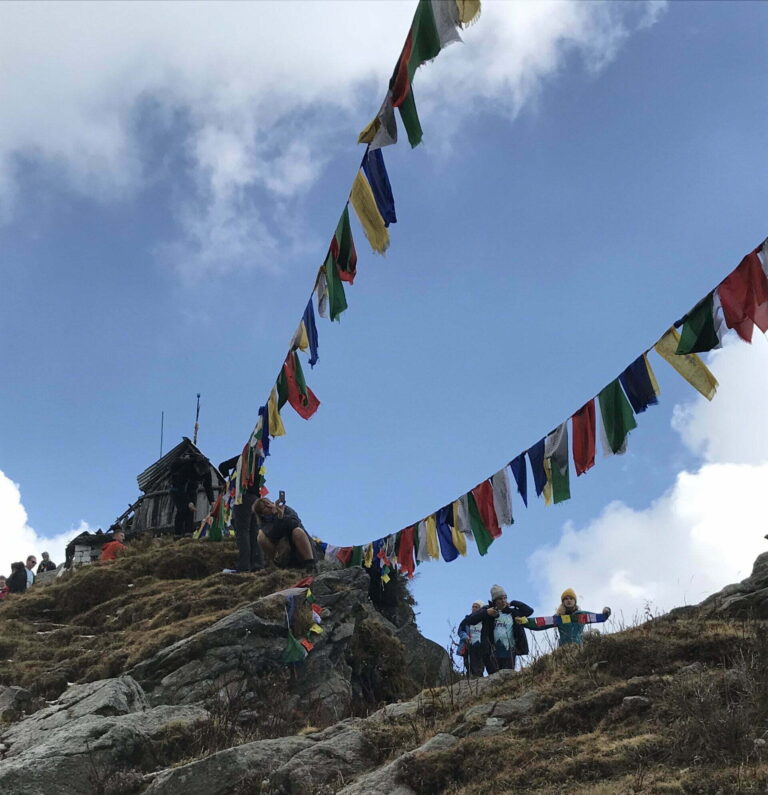 Trekkers walking on a rocky Himalayan trail with Tibetan prayer flags during the Dalai Lama Trek in Dharamshala