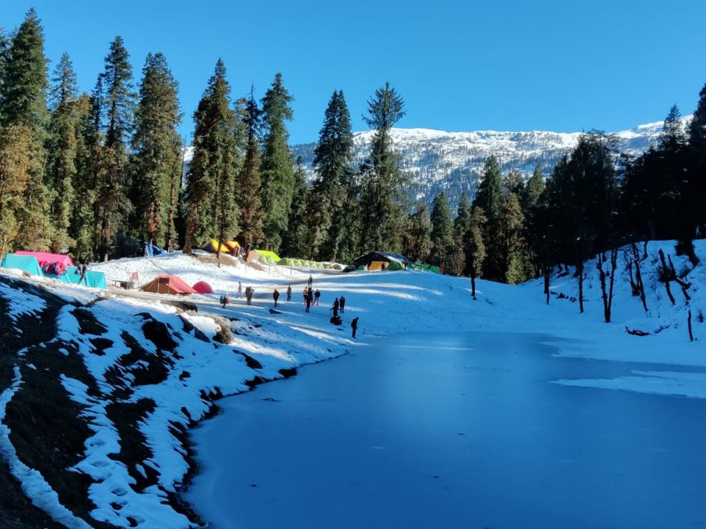 Frozen lake with snow campsite and trekking tents on the Kedarkantha trek in Uttarakhand
