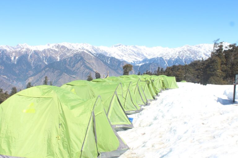 Snow campsite with green tents on the Kedarkantha trek in Uttarakhand Himalayas