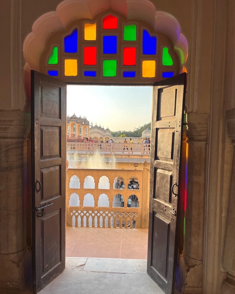 Golden Triangle Tour with Ranthambore Safari 2 View of Hawa Mahal through a traditional arched window with colorful stained glass in Jaipur Rajasthan