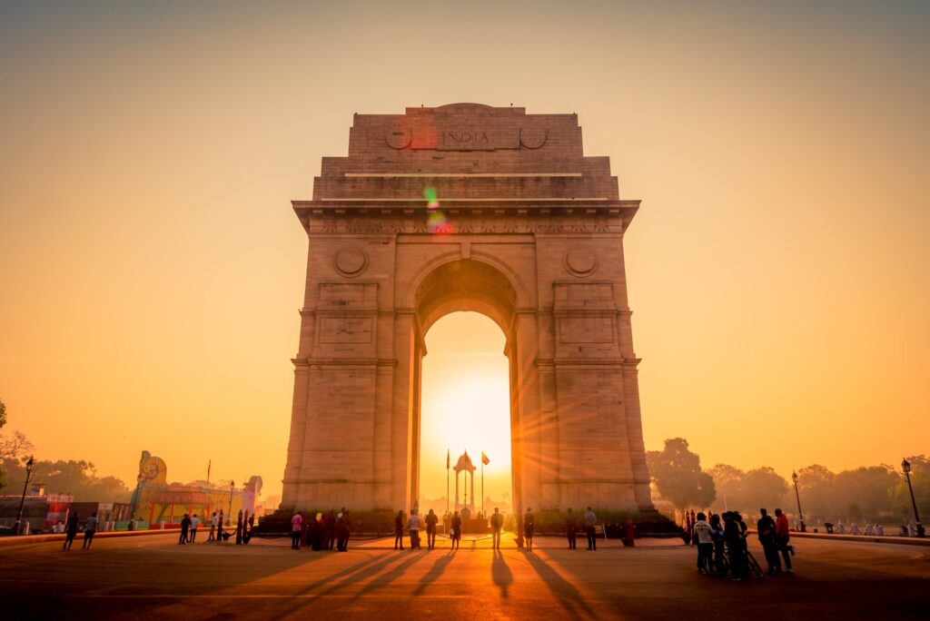 India Gate monument in New Delhi at sunrise with people walking around the memorial