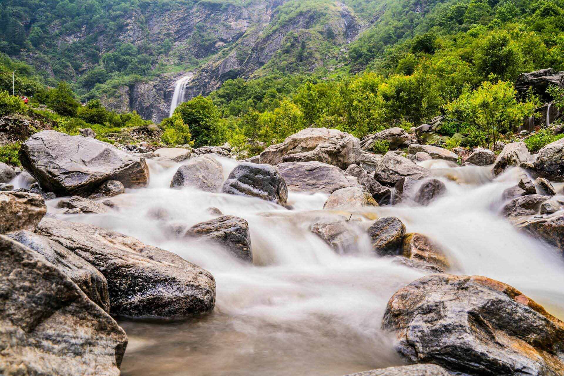 Mountain river flowing through rocks with a waterfall and green forest in the background.