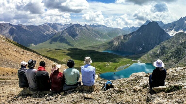 a group of people sitting on a mountain looking at a lake