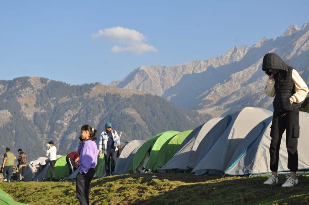 Trekkers camping at Thatharana meadow with panoramic Dhauladhar mountain views near Dharamshala