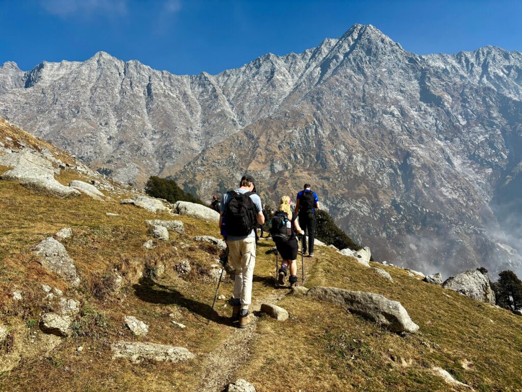 Trekkers walking on a rocky trail with Dhauladhar mountain range near Dharamshala