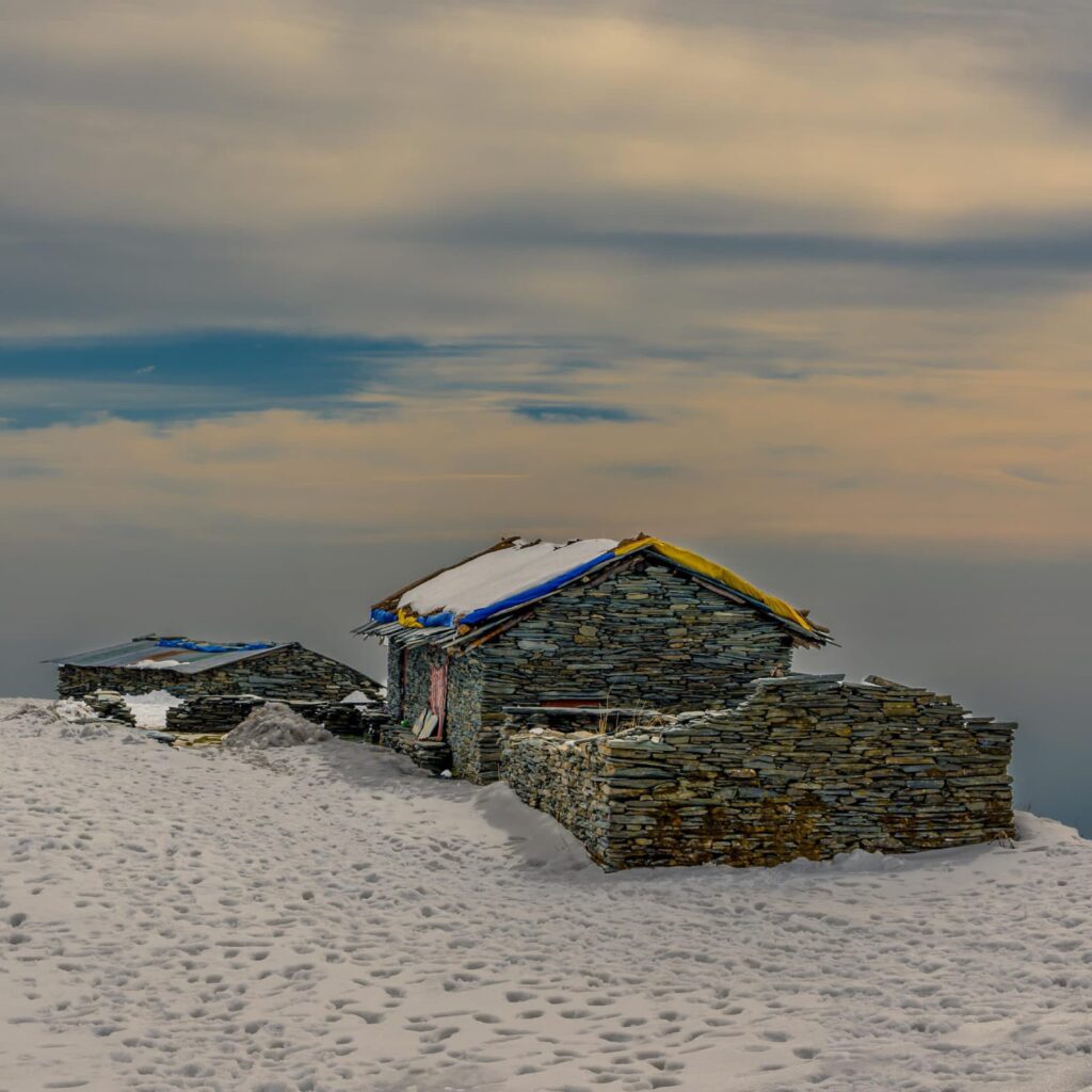 Traditional stone shepherd hut covered in snow during the Thatharana Trek near Dharamshala