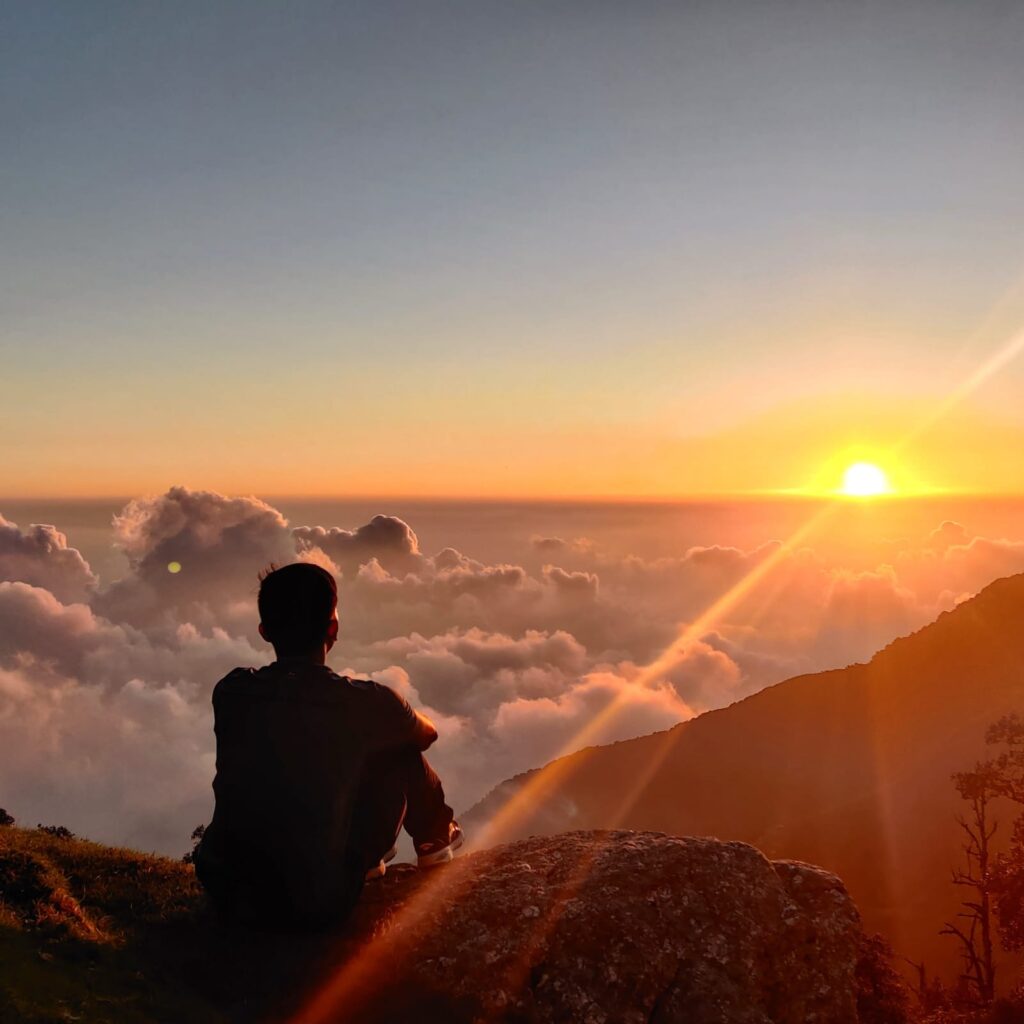 Trekker watching sunrise above the clouds during Thatharana Trek near Dharamshala