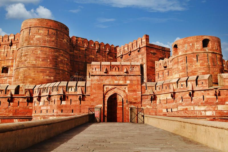 Front view of Agra Fort in Uttar Pradesh, India, showcasing its massive red sandstone walls, arched entrance, and Mughal architectural design under a bright blue sky.