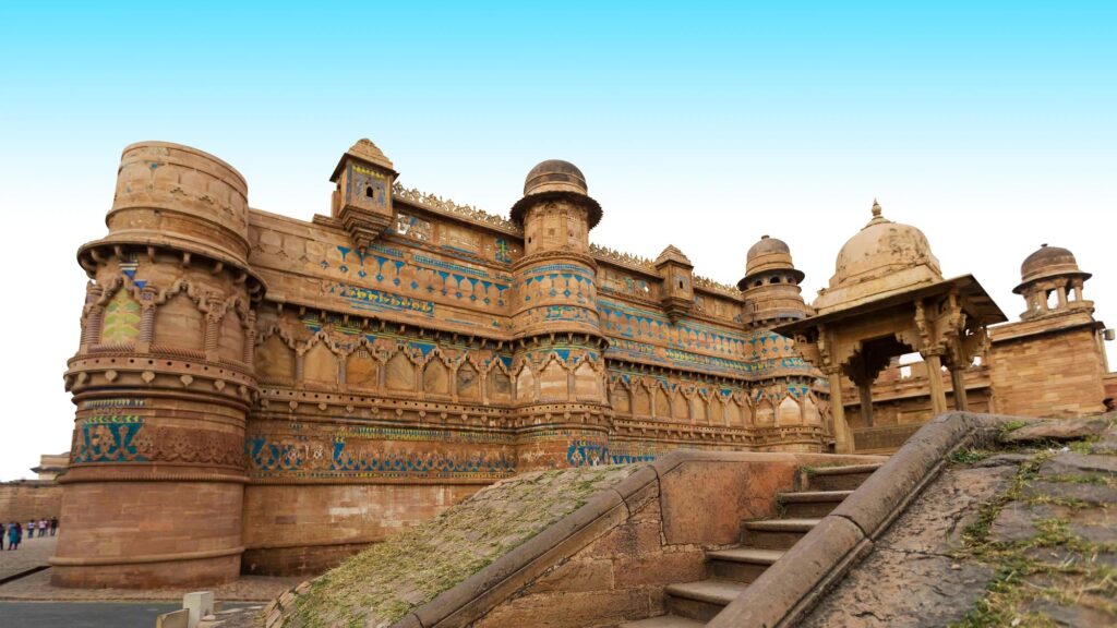 Front view of Gwalior Fort in Madhya Pradesh showcasing its sandstone walls, blue tile decorations, and intricate Rajput architecture under a clear sky.