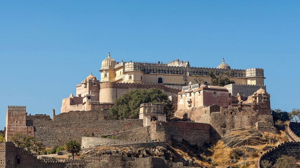 Panoramic view of Kumbhalgarh Fort in Rajasthan, India, featuring massive stone walls, bastions, and palace structures against a clear blue sky.