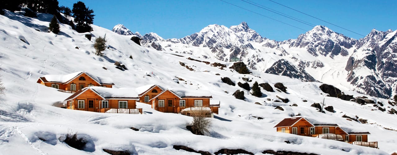 Gulmarg gondola cabins moving above snowy slopes with skiers and pine trees under bright winter sunlight in Jammu and Kashmir.