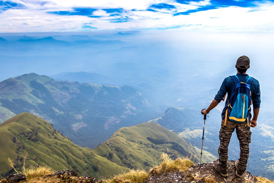 Solo trekker walking along a lush green mountain trail in India, symbolizing freedom, self-paced exploration, and the reassurance of guided support for solo travelers.