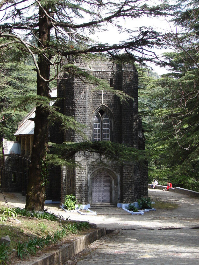 A historic stone church surrounded by tall deodar trees at St. John in the Wilderness, Dharamshala.