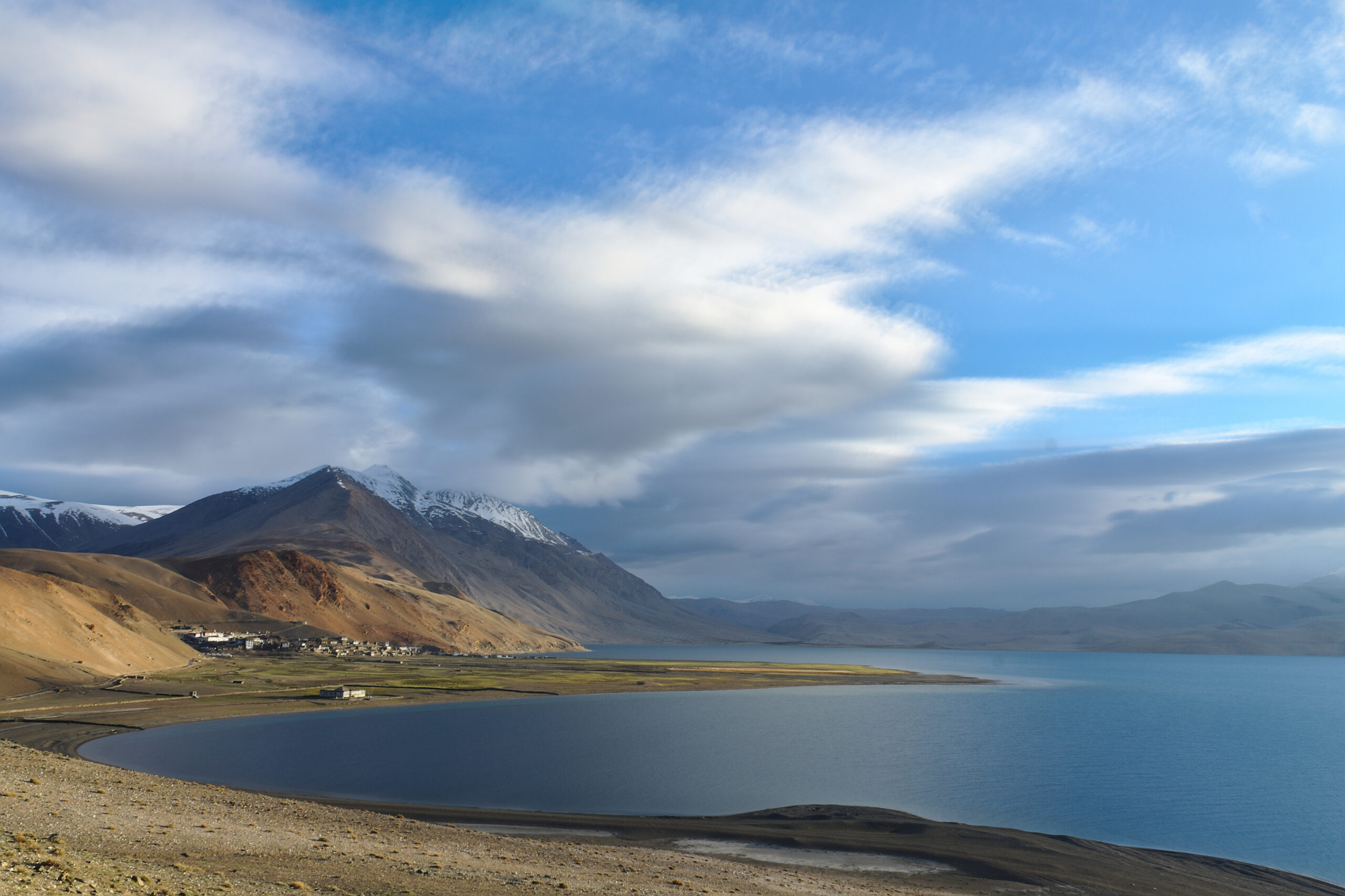 Scenic view of a high-altitude lake with snow-capped mountains and dramatic cloudy sky in Ladakh