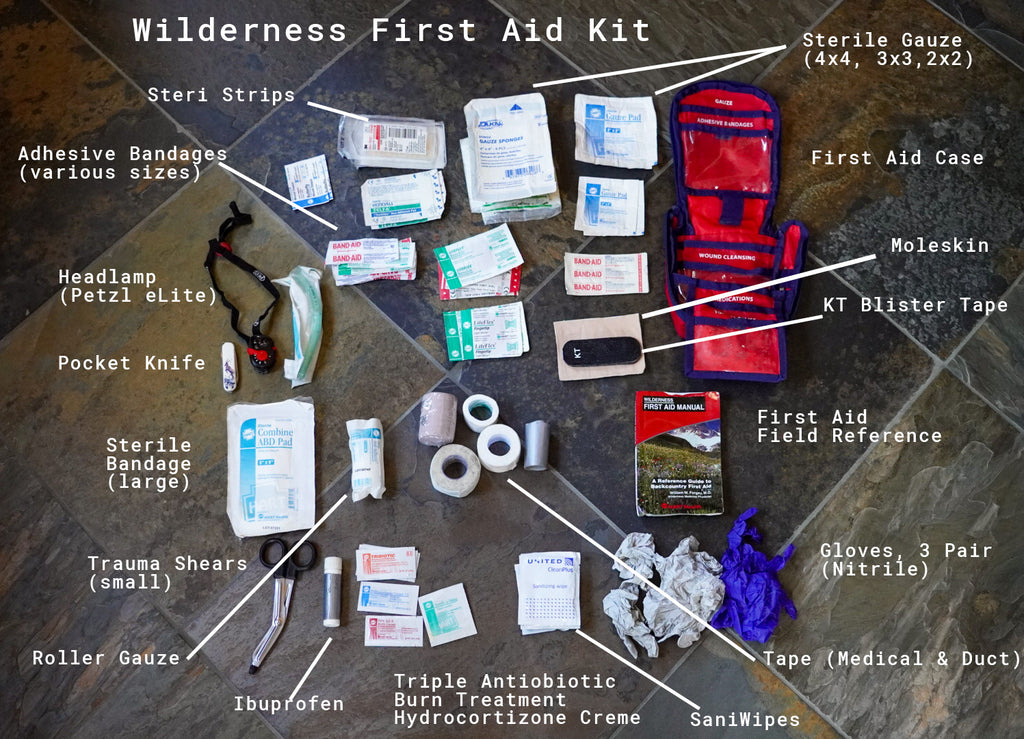 Wilderness first aid kit laid out with bandages, gauze, antiseptic, gloves, tape, scissors, and emergency medical supplies for mountain camping and trekking safety