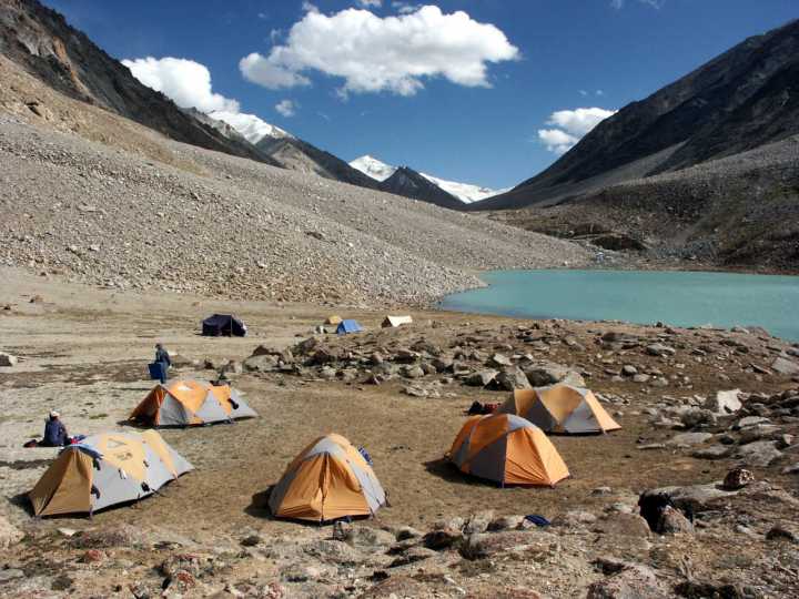 High-altitude Himalayan valley with rocky terrain, snow-capped mountains, and a glacial lake illustrating remote mountain camping terrain