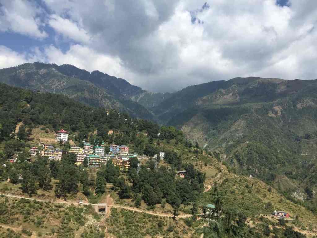 Scenic landscape view of McLeod Ganj and Dharamshala with mountains, green forests, and hillside houses under a cloudy sky