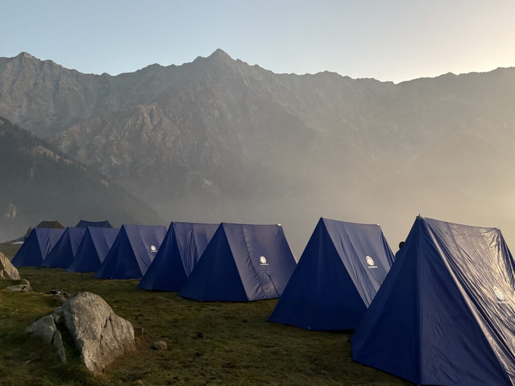 Blue trekking tents lined up beneath a dramatic mountain ridge