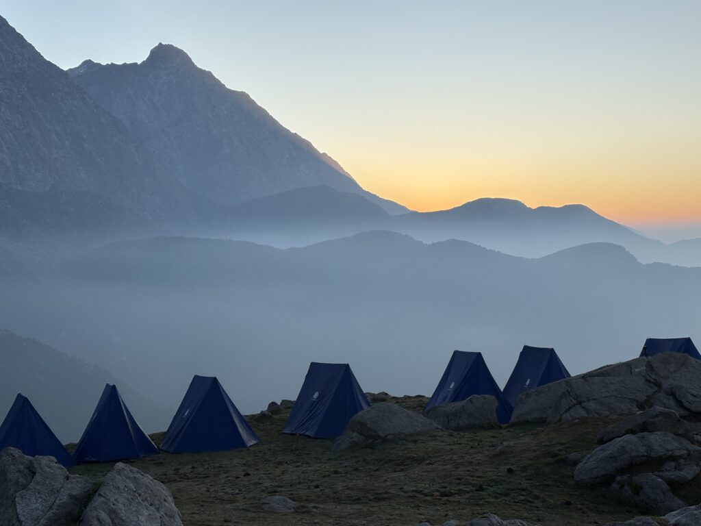 Blue tents overlooking layered mountain ridges beneath a golden sunset