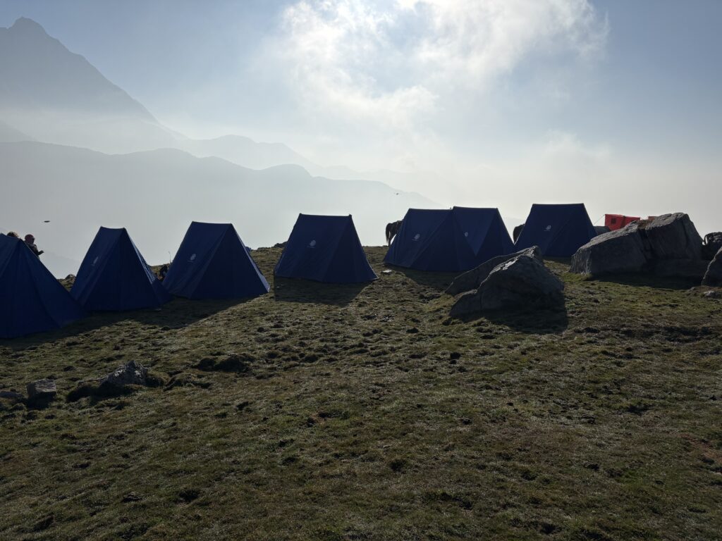 Blue trekking tents on a grassy mountain campsite beneath misty ridgelines