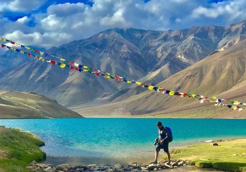 a man standing on a rocky shore next to a lake with colorful flags