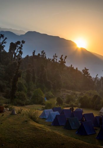 a group of tents in a field with mountains in the background