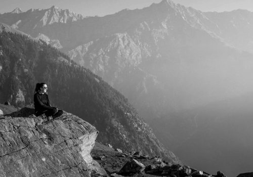 a woman sitting on a rock with mountains in the background