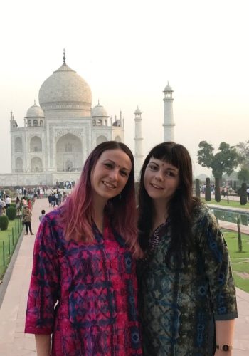 two women standing in front of a large building with Taj Mahal in the background