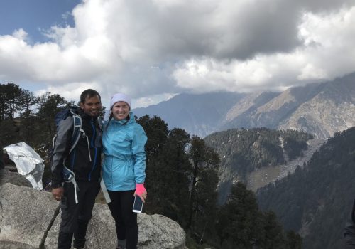 a man and woman standing on a rock with mountains in the background