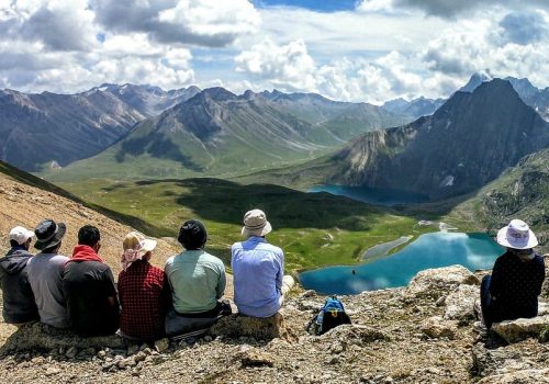 a group of people sitting on a mountain looking at a lake