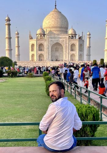 a man sitting on a bench in front of a large white building with Taj Mahal in the background