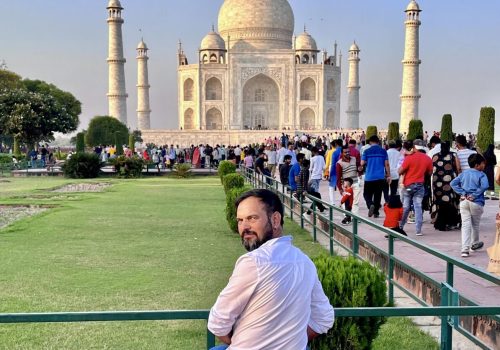 a man sitting on a bench in front of a large white building with Taj Mahal in the background